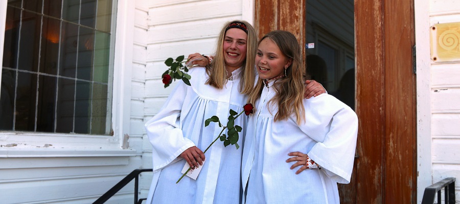 To ungdommer i hvite kapper står smilende på en trapp etter konfirmasjonen. Foto.